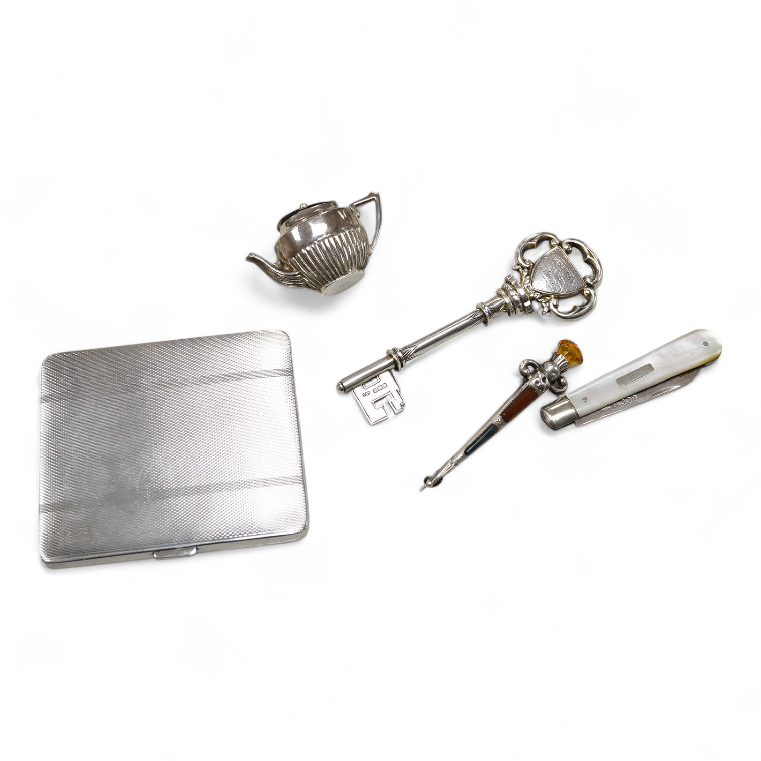 A George V silver presentation key, Vaughton & Sons, Birmingham, 1910, 10.2cm, together with a silver cigarette case, a silver and mother of pearl fruit knife, a miniature 925 demi-fluted teapot and a Scottish hardstone
